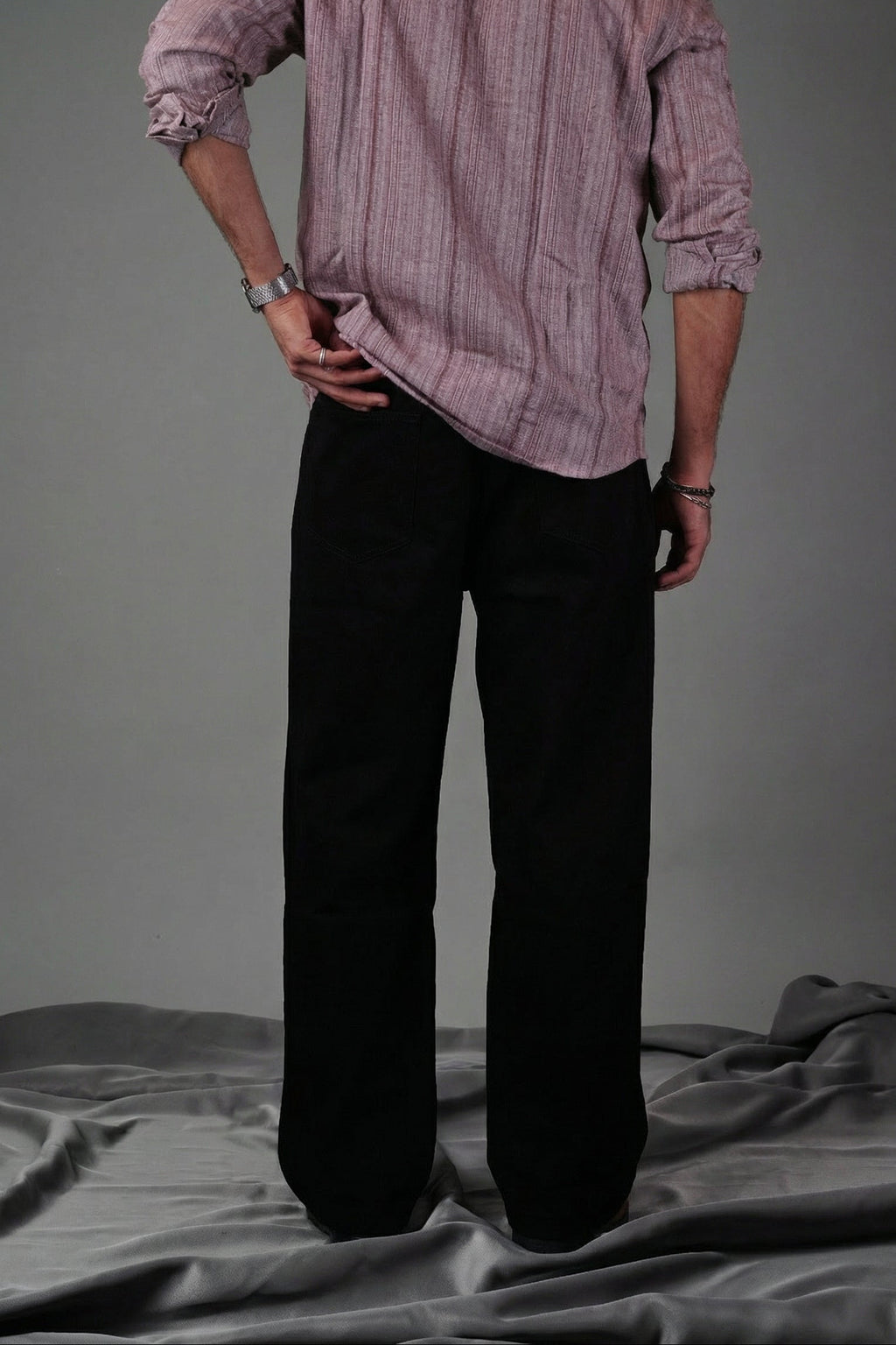 Person wearing a light pink shirt and dark pants standing against a gray background
