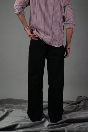 Person wearing a light pink shirt and dark pants standing against a gray background