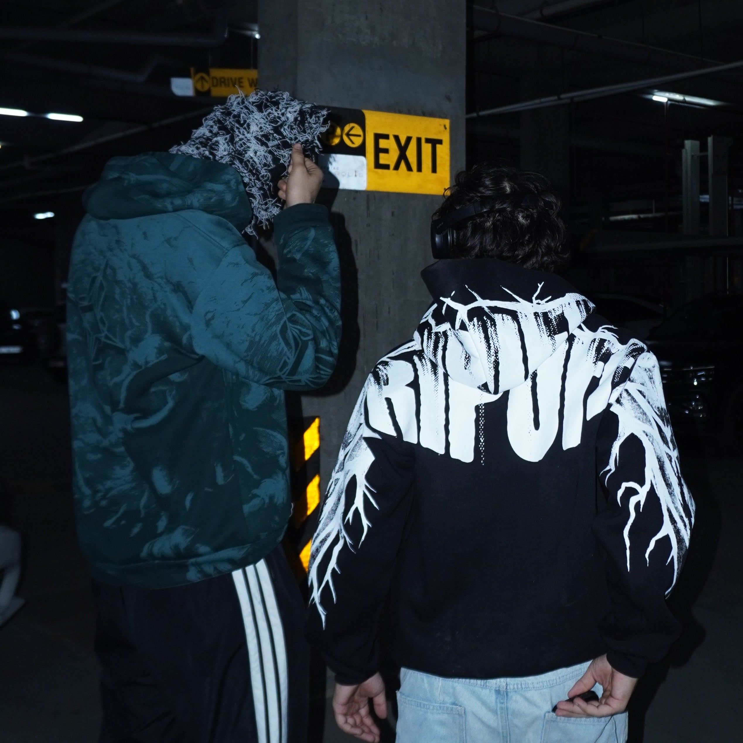 Two people in a dark indoor setting with one wearing a hoodie with 'ripoff' text.
